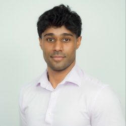 Dr SJ Siva Headshot, wearing white button up standing against blank white wall